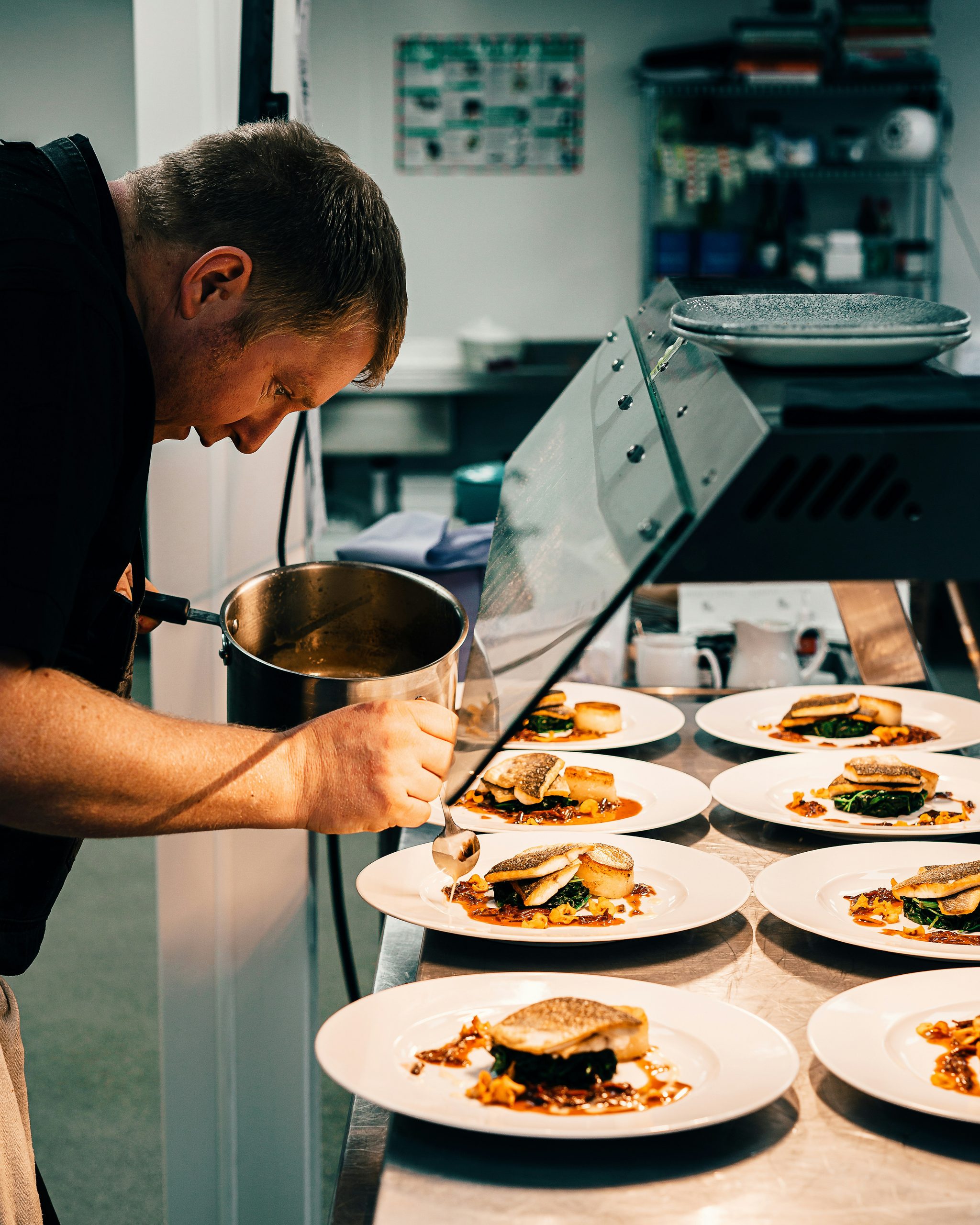 Chef finishing a row of plated dishes in a catering kitchen before service